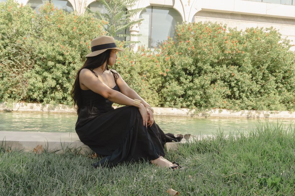 A fashionable woman in a sun hat sitting by a pond in Baku park, embodying summer relaxation and style.