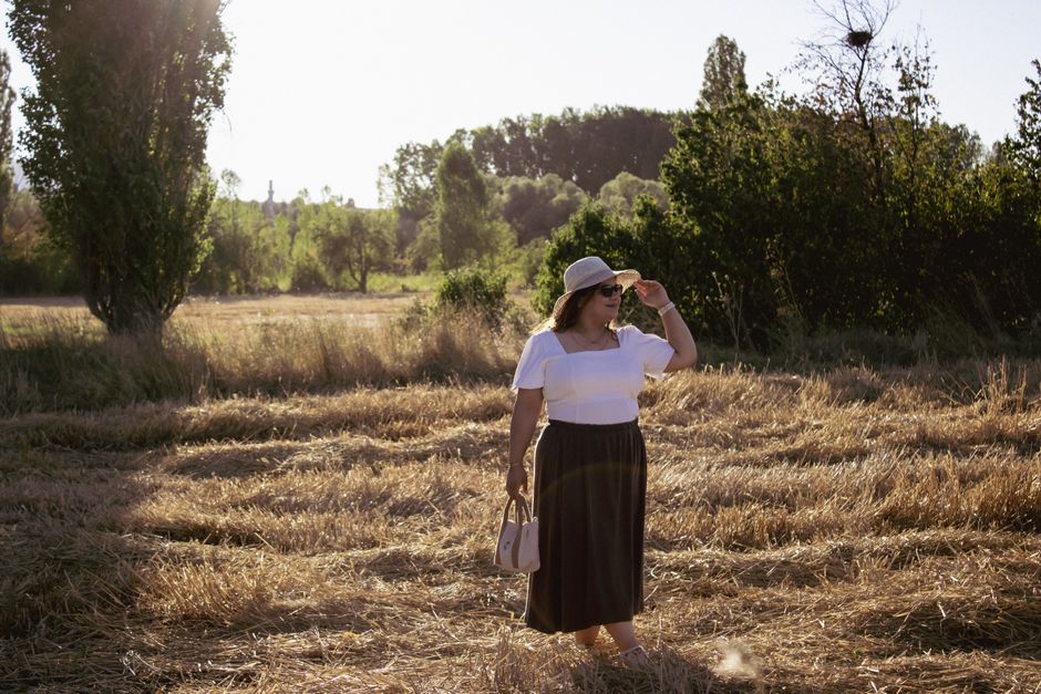A woman in a hat stands in a sunlit field, enjoying the serene early summer atmosphere.