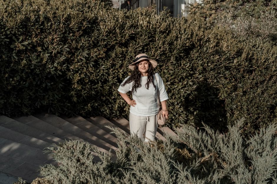 A woman wearing a sun hat poses outside surrounded by lush greenery in Baku.