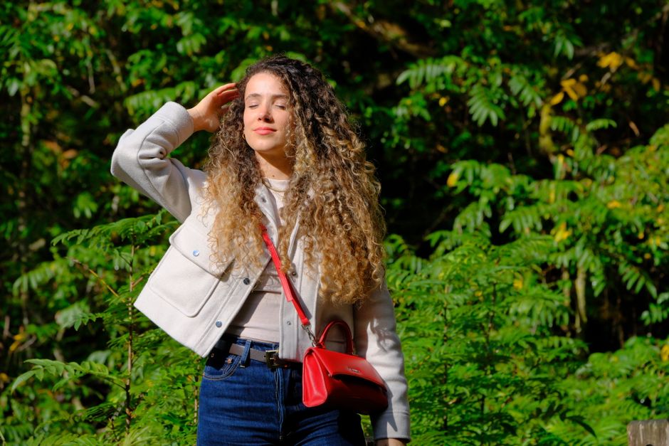 Young woman with curly hair enjoying sunlight in a green outdoor setting.