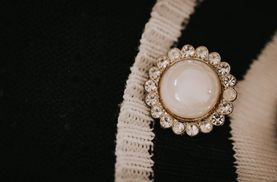 Close-up of a vintage brooch with white center and gems on textured black and white fabric.