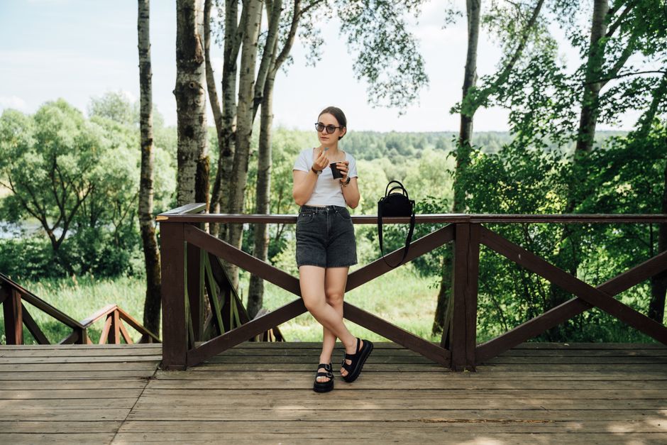 Woman in casual summer outfit enjoying coffee outdoors, surrounded by lush greenery.