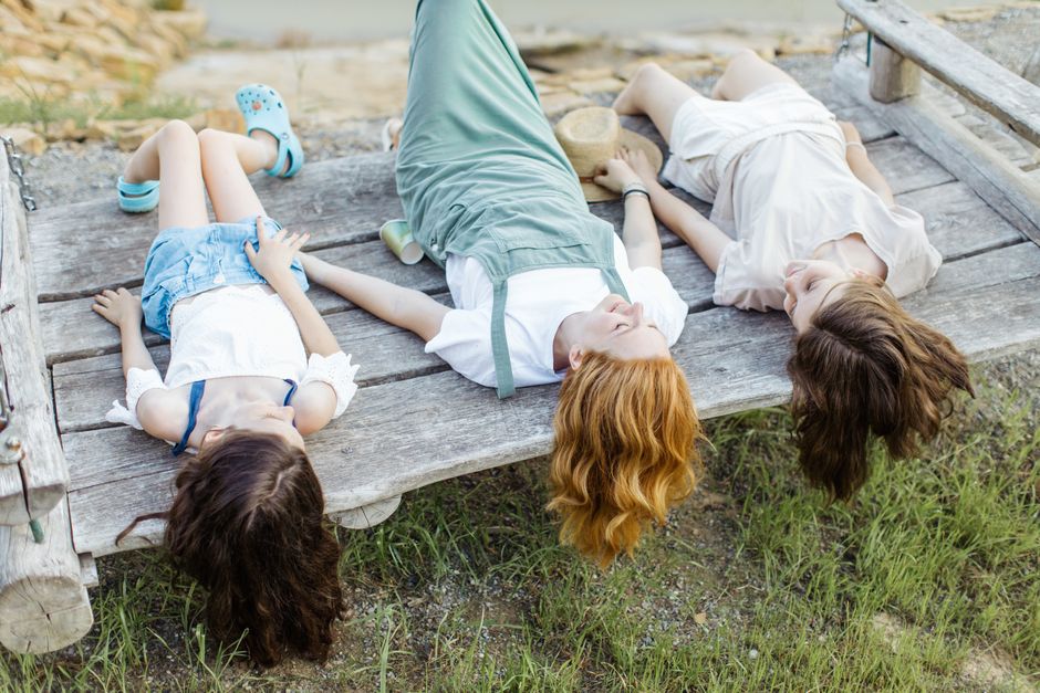 Three young women lying back on a wooden bench, enjoying a peaceful day outdoors.