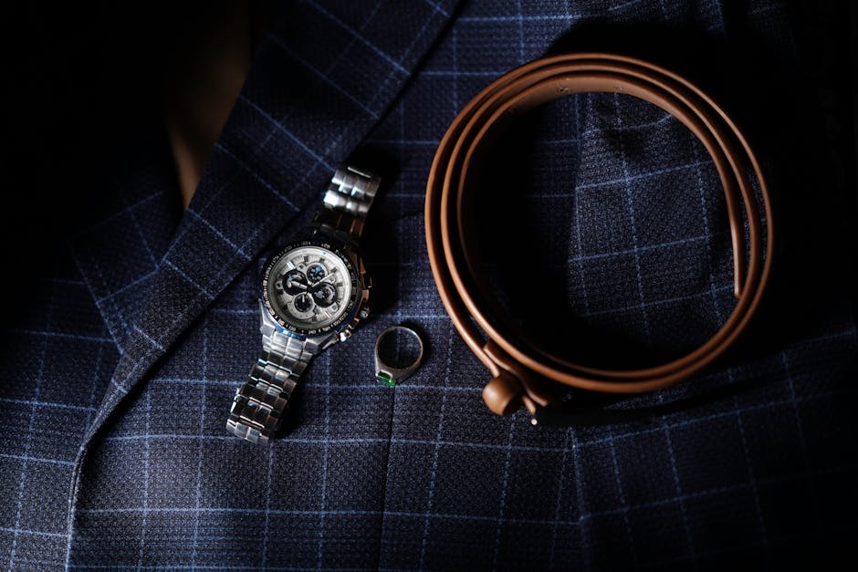 Stylish men's accessories including a wristwatch, leather belt, and silver ring on a plaid blazer.