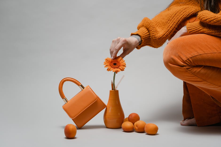 A minimalist composition featuring a woman arranging an orange flower in a vase with matching accessories.