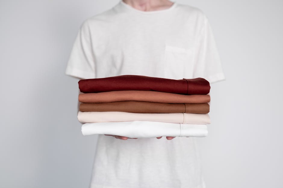 Minimalist close-up of folded neutral-colored shirts held by a person.