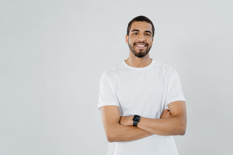 Confident man with arms crossed wearing a white t-shirt and smartwatch, smiling.