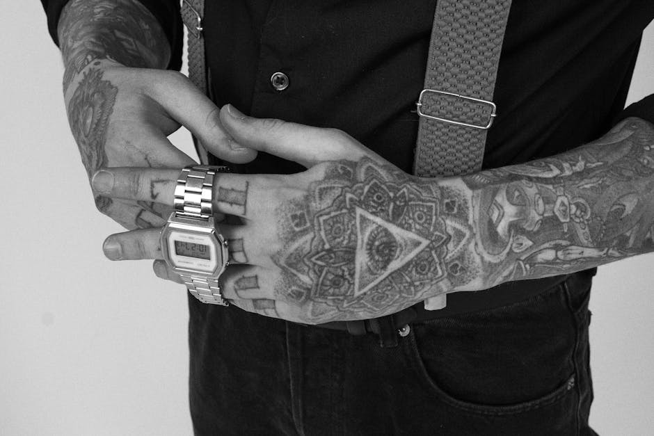 Close-up of tattooed hands in black and white, featuring a silver watch and suspenders.