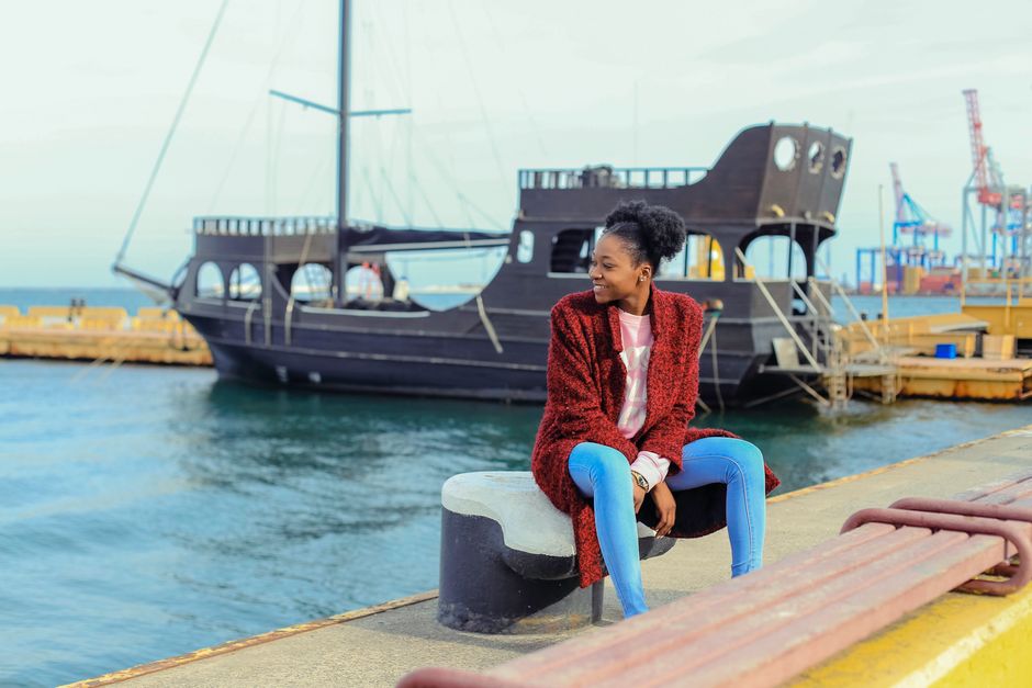 A woman sitting by Odesa harbor enjoying the view. A ship and cranes are visible in the background.
