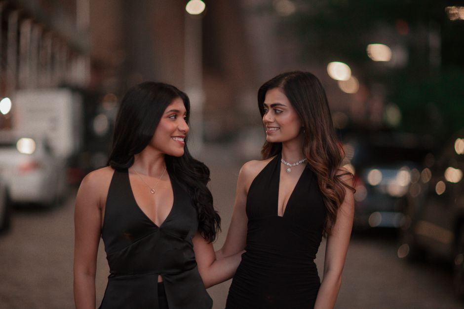 Two women in elegant black dresses smiling during an evening stroll outdoors.