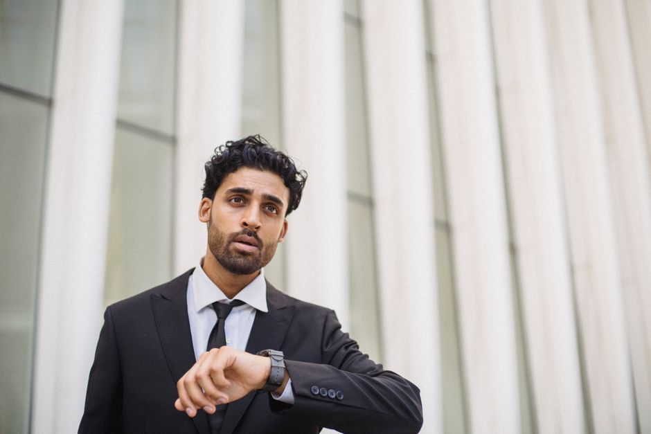 A professional man in a suit checks the time on his watch while standing outside, capturing a business theme.