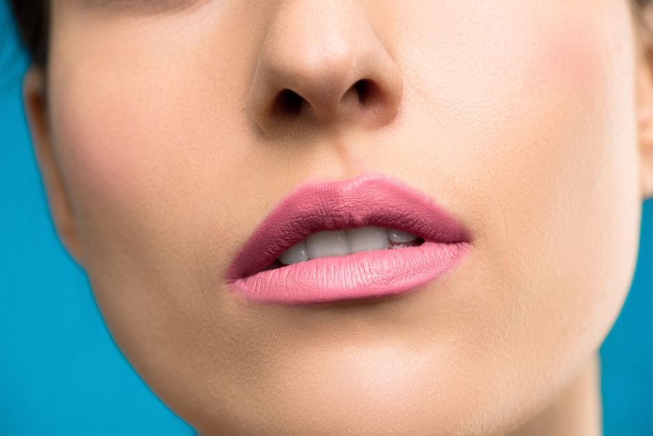 Detailed close-up of woman's lips and skin with vibrant pink lipstick on a blue background.