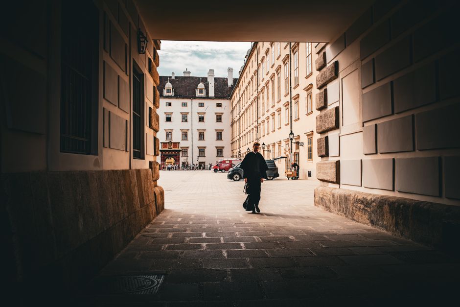 A person walking through a historic European courtyard framed by an archway.