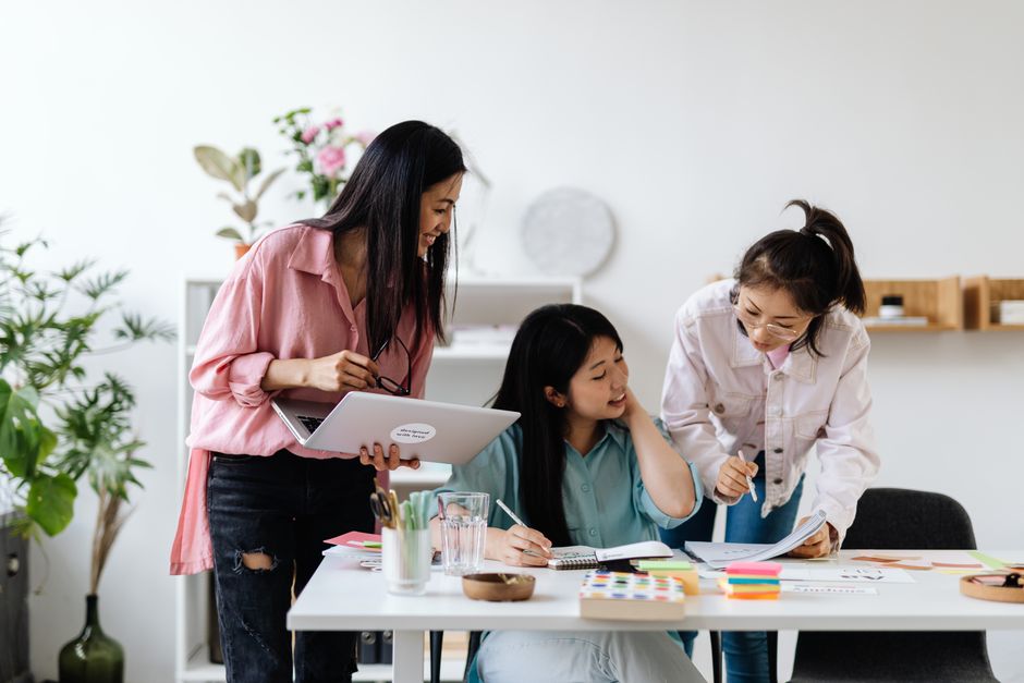 Three women brainstorming and collaborating in a modern office setting.