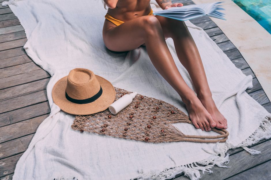 Woman reading by the poolside with a sun hat, creating a summer vibe.