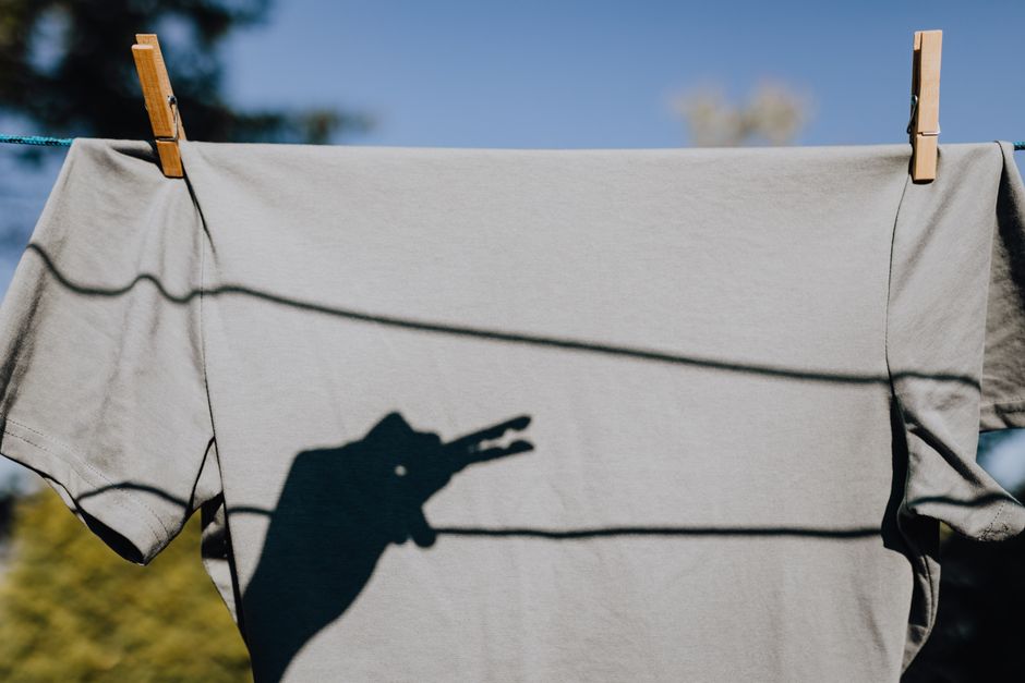 Clean tee shirt with shadow of hand with clothespin of anonymous person showing shade of crocodile in backyard during cloudless sunny day