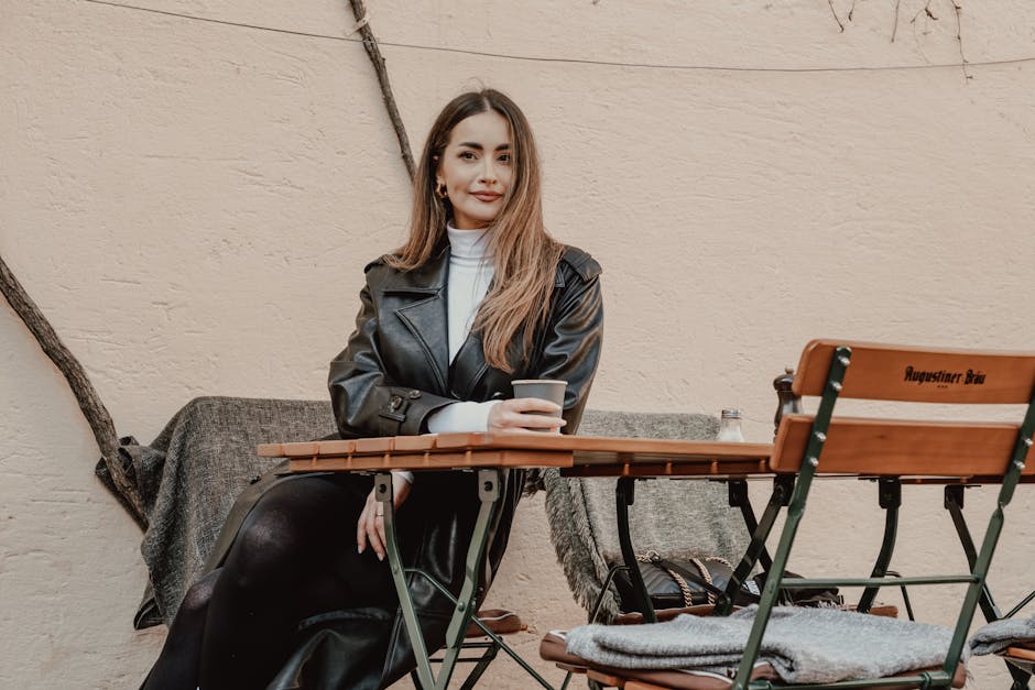 Woman in a leather jacket enjoying a coffee at an outdoor cafe table.