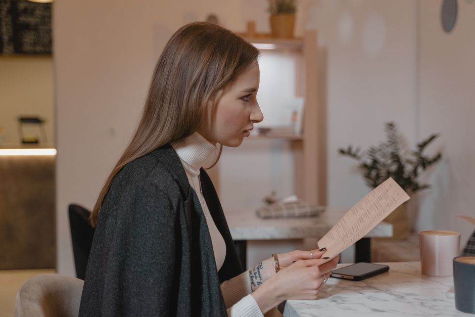 Side view of woman holding menu in a cozy café setting, wearing a turtleneck and jacket.