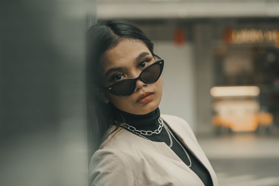 A fashionable adult woman wearing sunglasses posing confidently in an urban setting.