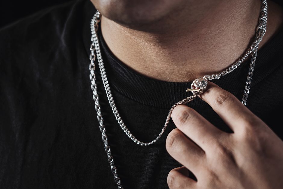 Close-up of a man displaying a stylish silver necklace with pendant, highlighting its intricate design.