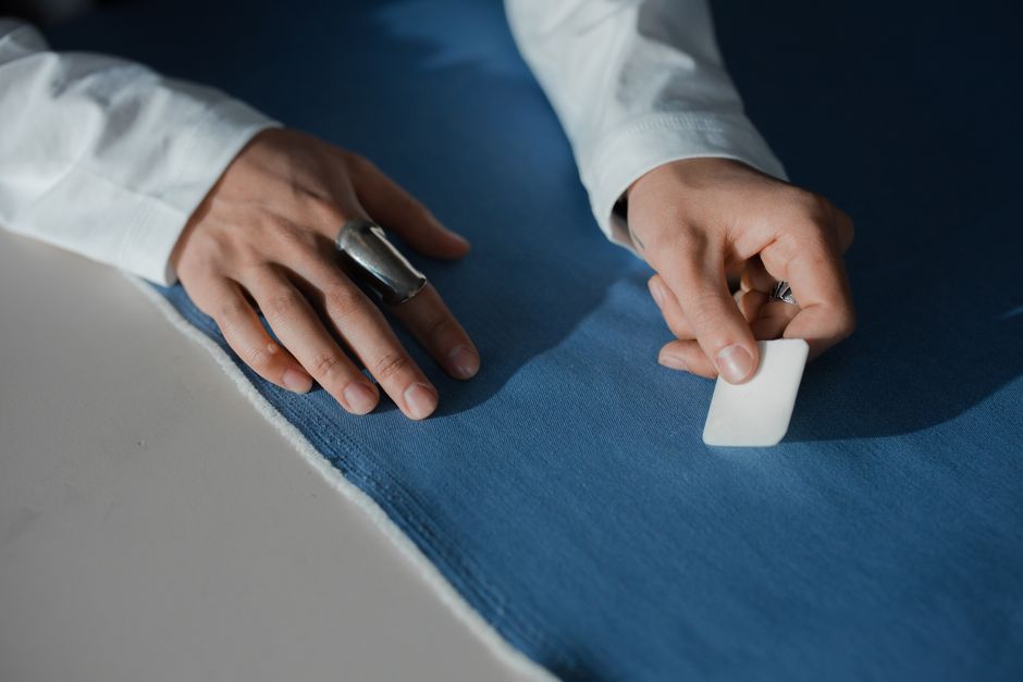 Detailed close-up of hands marking blue fabric with tailor's chalk, focused on tailoring and dressmaking process.