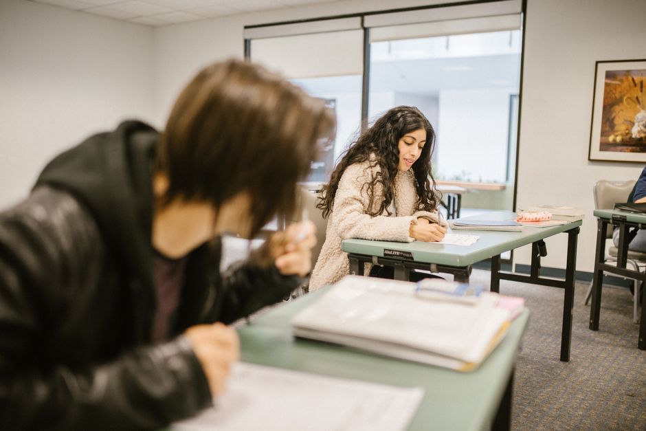 Two students focused on an exam in a classroom setting during daylight.