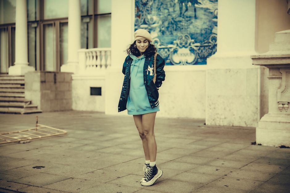 Stylish woman wearing a hoodie and cap stands against an urban backdrop, exuding modern street fashion.