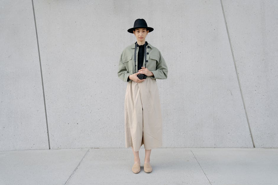 Fashionable woman in minimalist attire holding camera, standing against a concrete wall.