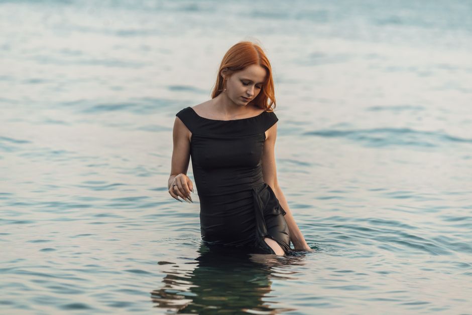 Young woman in black dress standing in sea, exuding peace and contemplation.