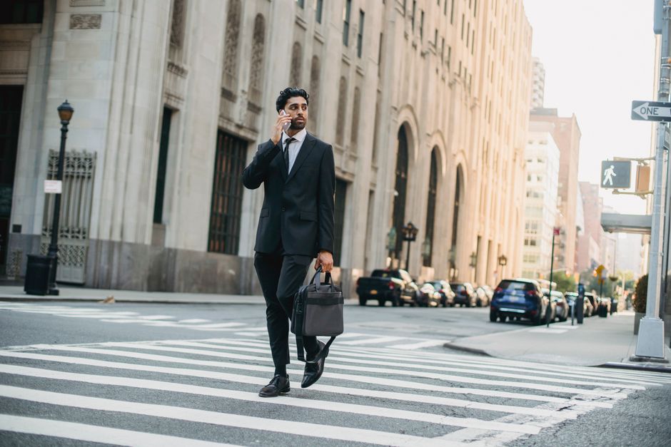 Confident businessman in suit talking on phone while crossing city street.