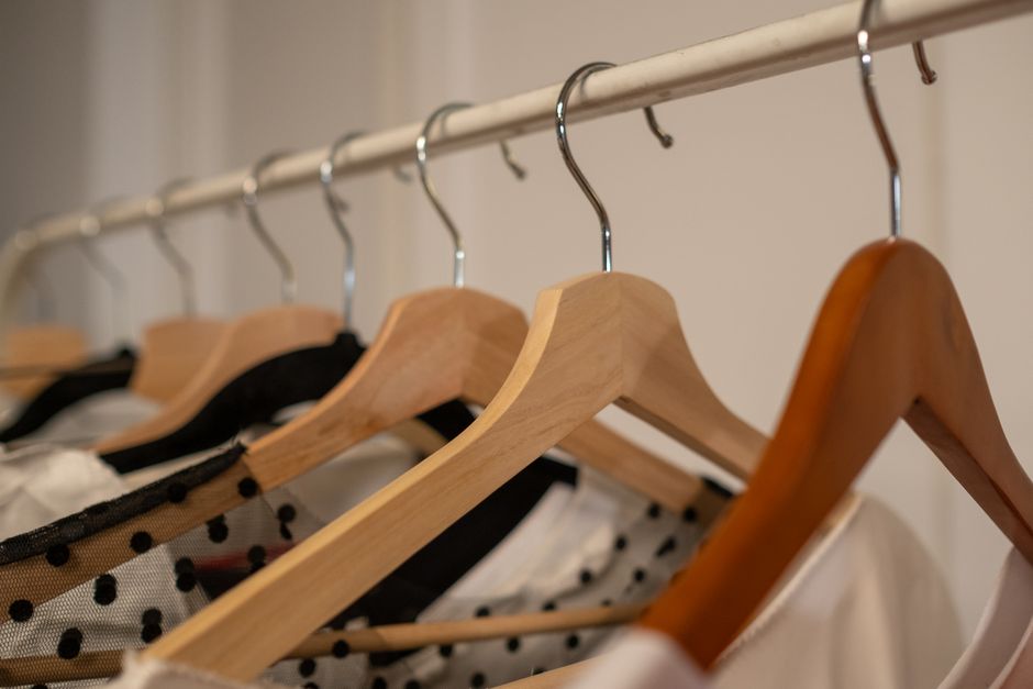 Close-up of wooden clothes hangers with assorted clothing indoors.