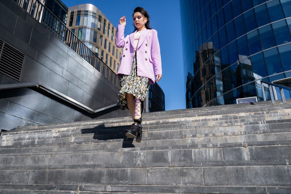 Stylish woman with prosthetic leg descends city steps in vibrant attire on a sunny day.