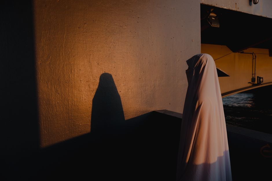 A woman in traditional dress casts a shadow on a wall at sunset, creating a dramatic silhouette.