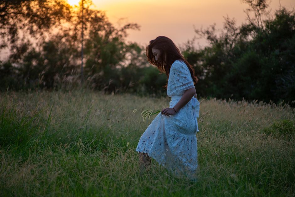 A woman walks through a grassy meadow during a peaceful sunset, capturing a moment of serene beauty.