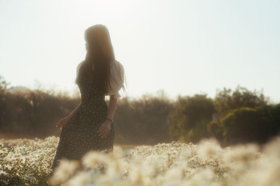 A serene silhouette of a woman standing in a sunlit flower field, creating a peaceful autumn scene.