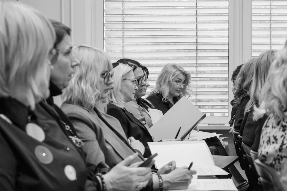 Black and white image of women in a meeting, attentively taking notes.