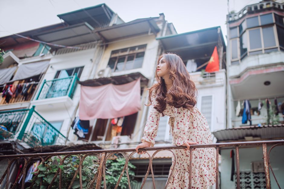 Stylish woman with long hair leans on railing in a lively urban area.