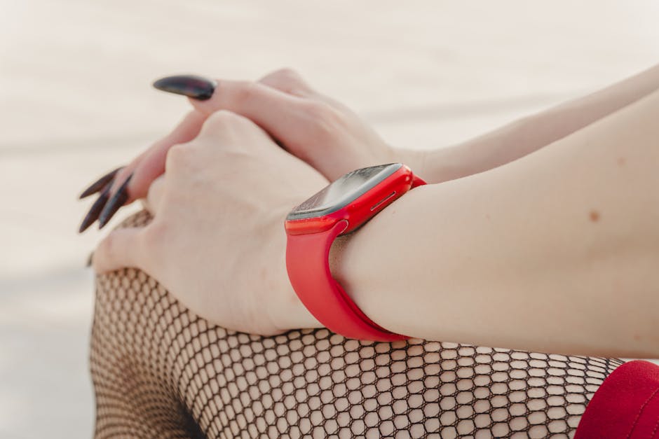 Hands resting with a red smartwatch, wearing fishnet stockings, showcasing casual style.