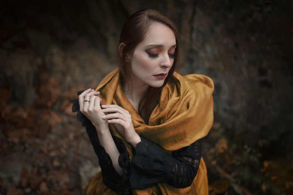 Artistic portrait of a woman in a yellow scarf with vivid eyeshadow, in an outdoor setting with autumn leaves.