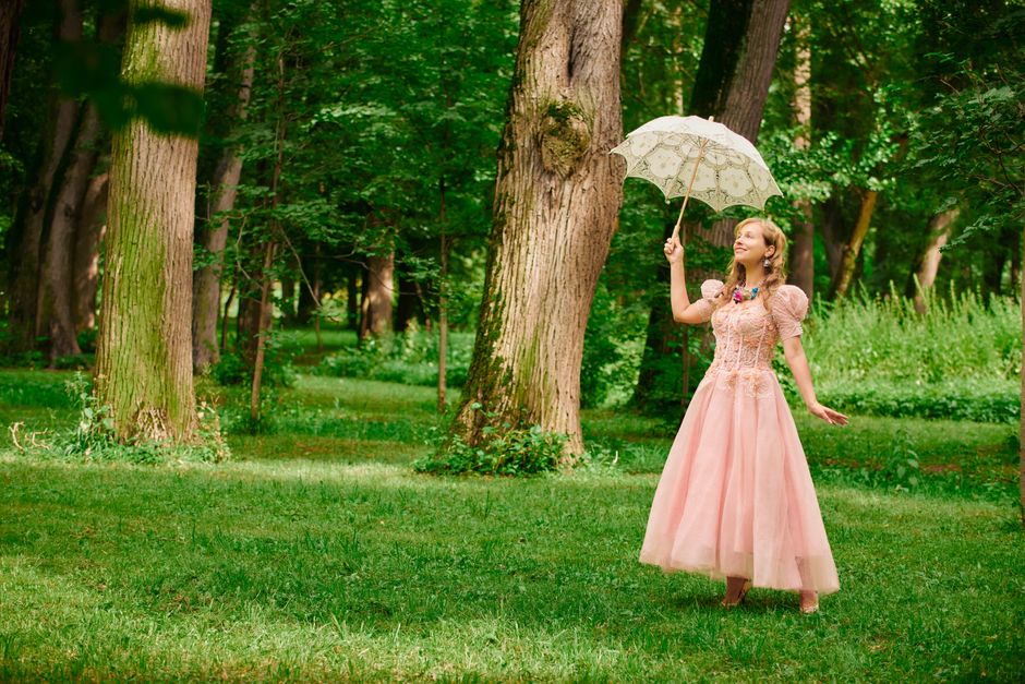 A woman in a vintage pink dress holding a parasol in a lush green forest.