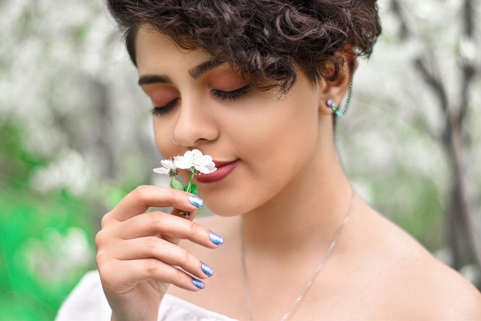 A woman with curly hair smiling while smelling white flowers outdoors in spring.