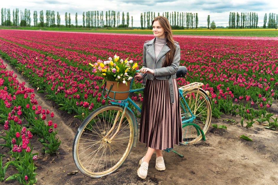 Young woman in stylish outfit with bicycle and flowers in a lush tulip field.