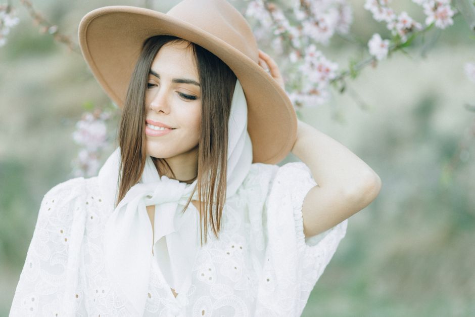 A serene portrait of a woman in a brown hat surrounded by springtime blossoms, exuding tranquility.