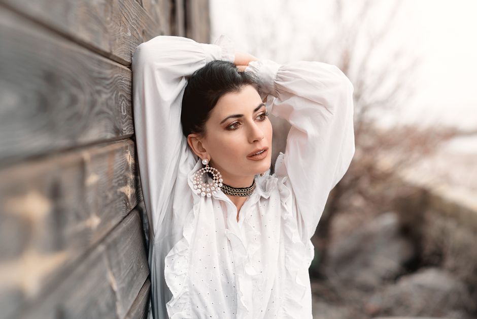 Woman posing stylishly in a white blouse, exuding elegance and confidence beside a wooden wall.
