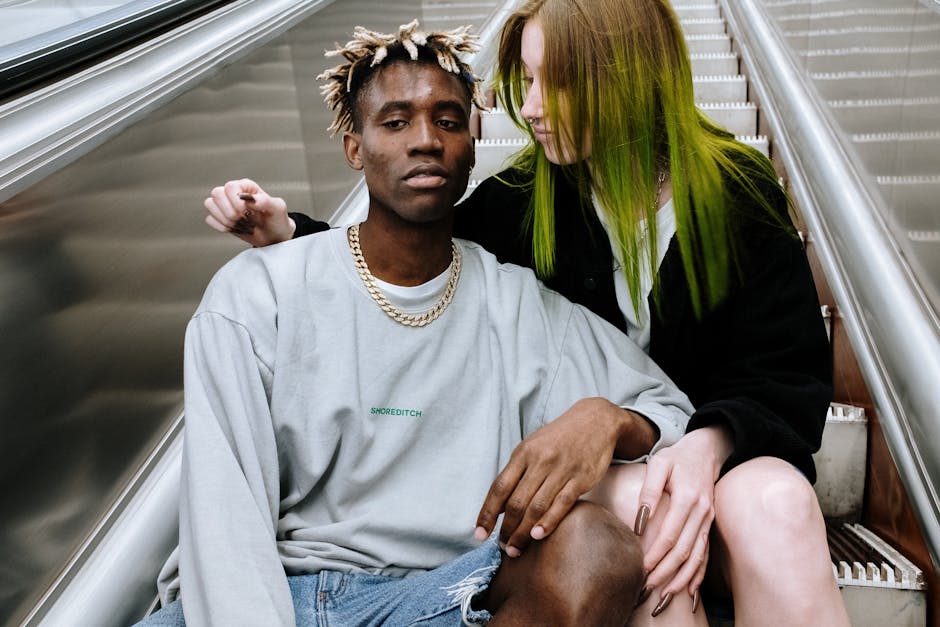 Trendy couple with striking hairstyles sitting on an urban escalator showcasing modern fashion.