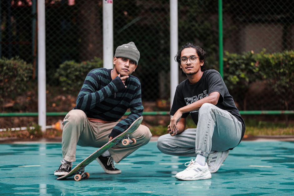 Two stylish young men crouching and posing with a skateboard, showcasing street fashion and youthful energy.