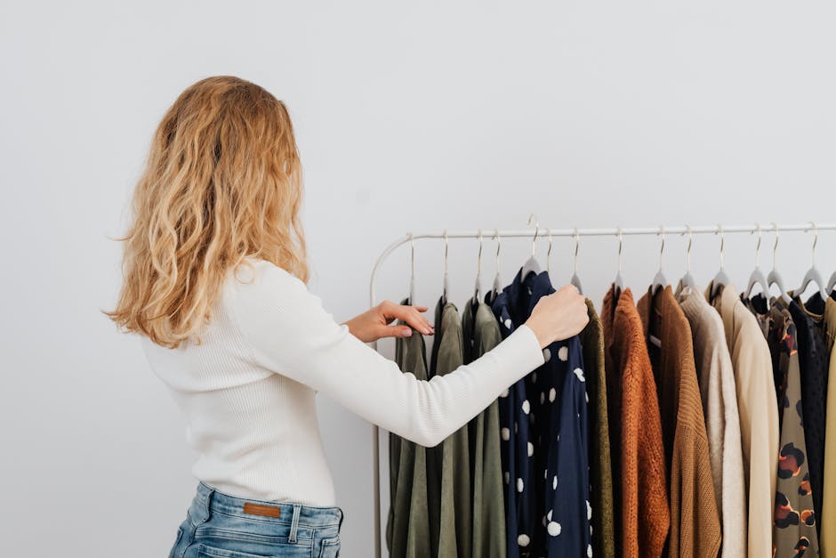 A woman browsing clothing rack in a modern boutique, wearing a white sweater.