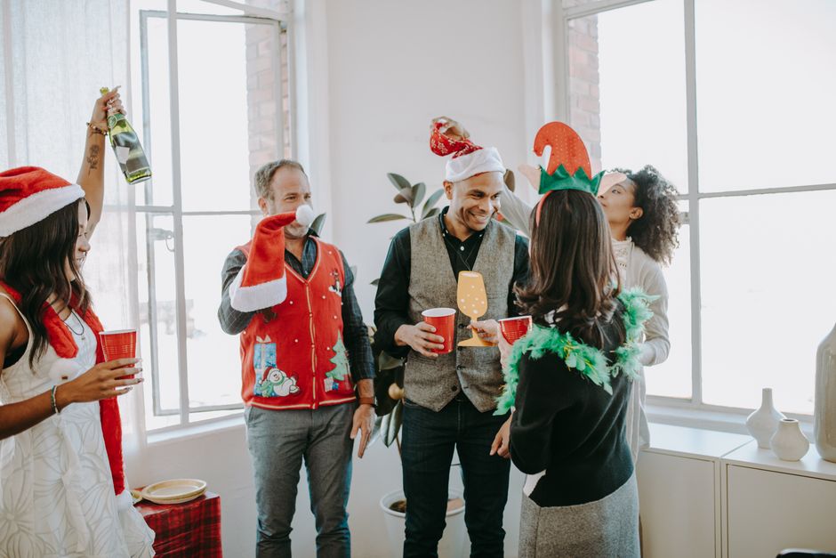 Colleagues celebrating a festive holiday party in an office setting, enjoying drinks and wearing fun costumes.