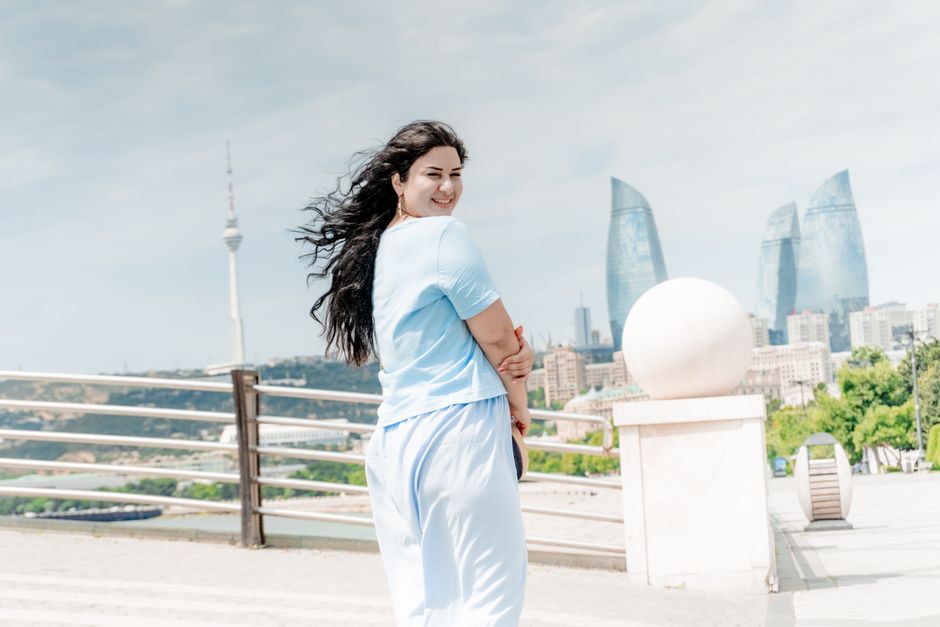 A woman smiles with Baku's iconic Flame Towers in the background under a clear sky.