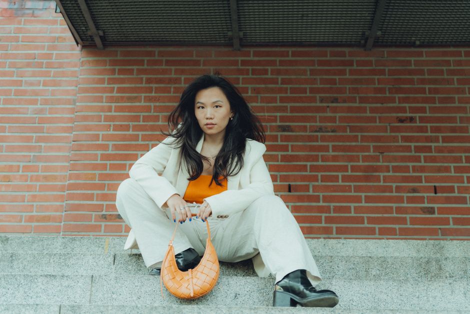 Stylish woman in white suit with orange blouse sitting on city steps holding a handbag.